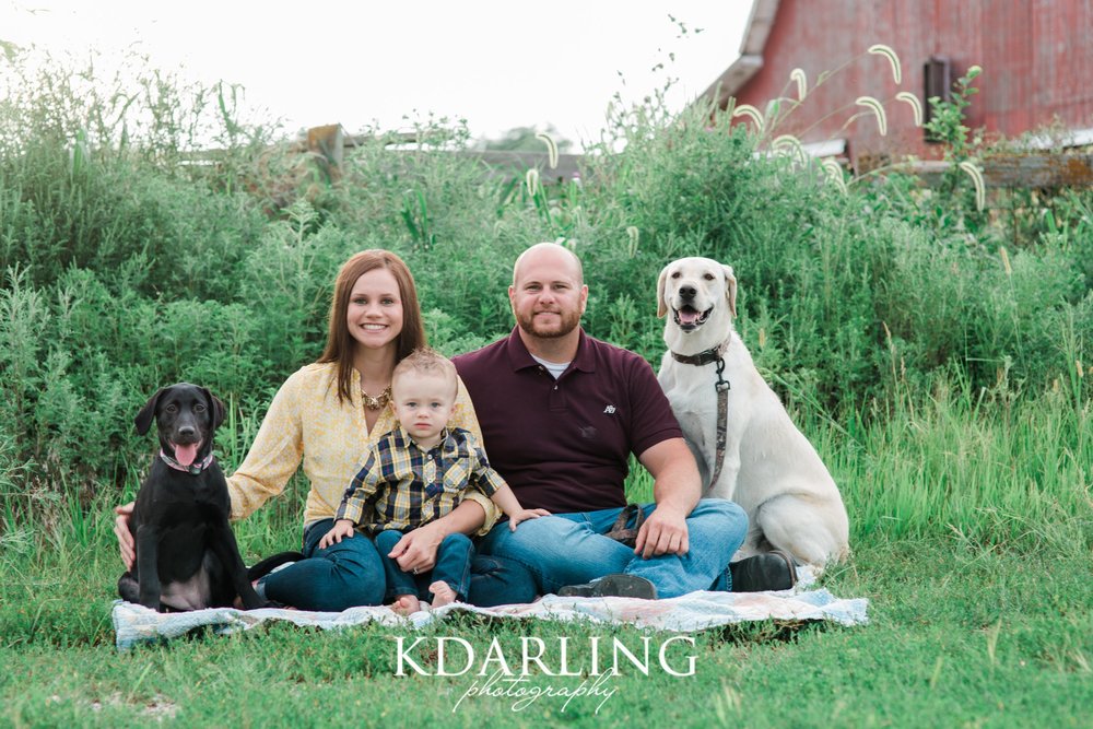 family of 3 with 2 dogs and red barn