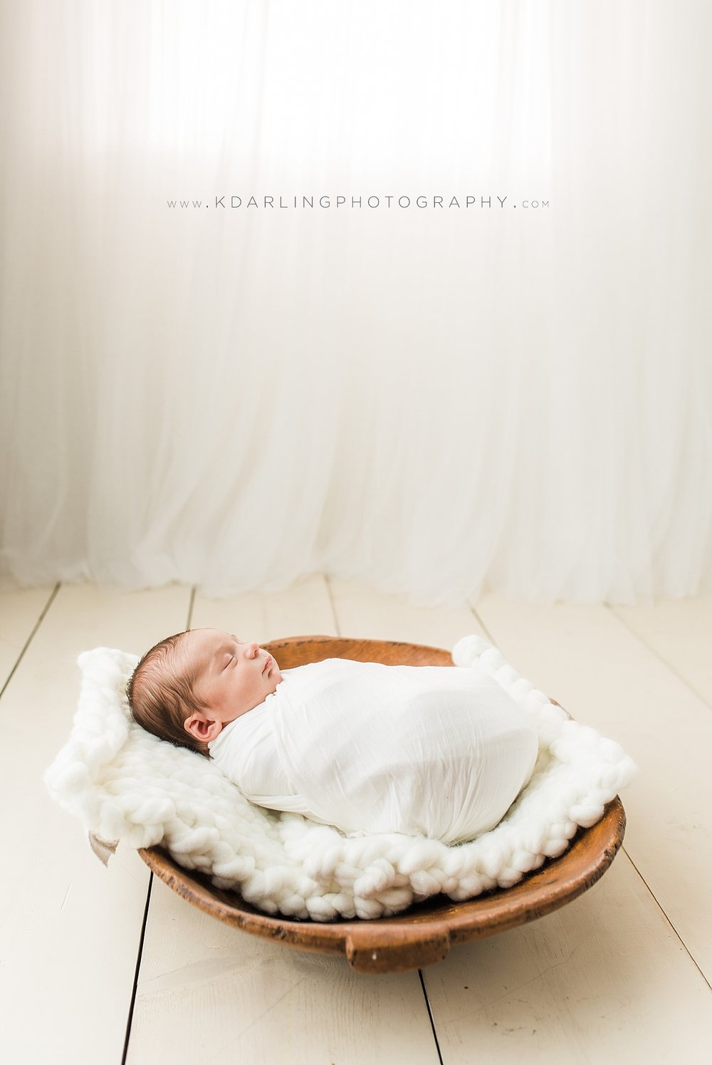 Newborn baby wrapped in white on wood floor