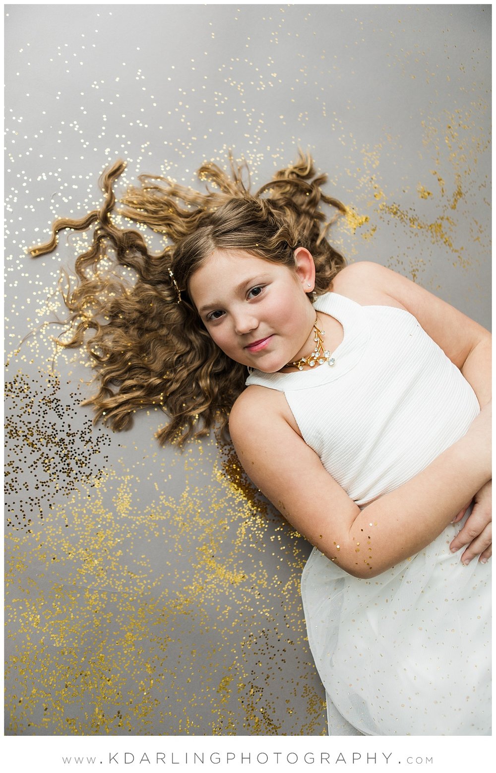 Tween girl in white dress laying in glitter