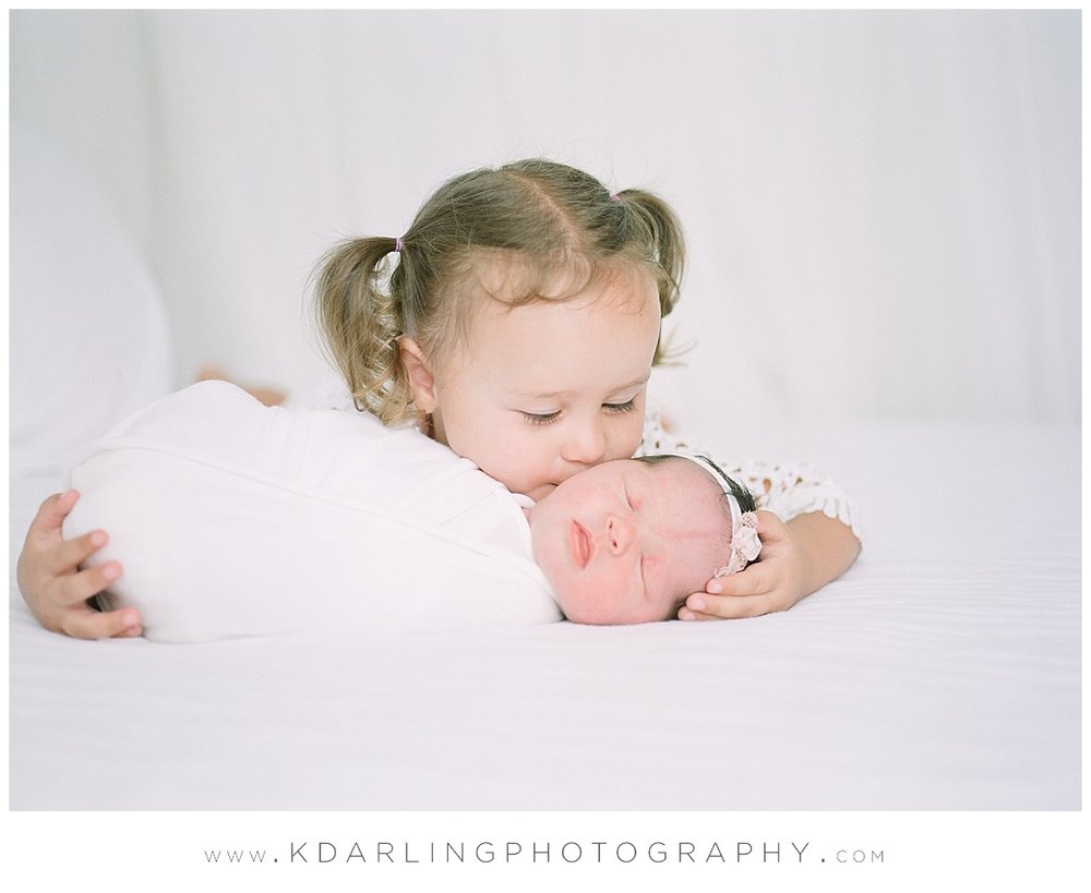Big sister kisses baby at newborn session.