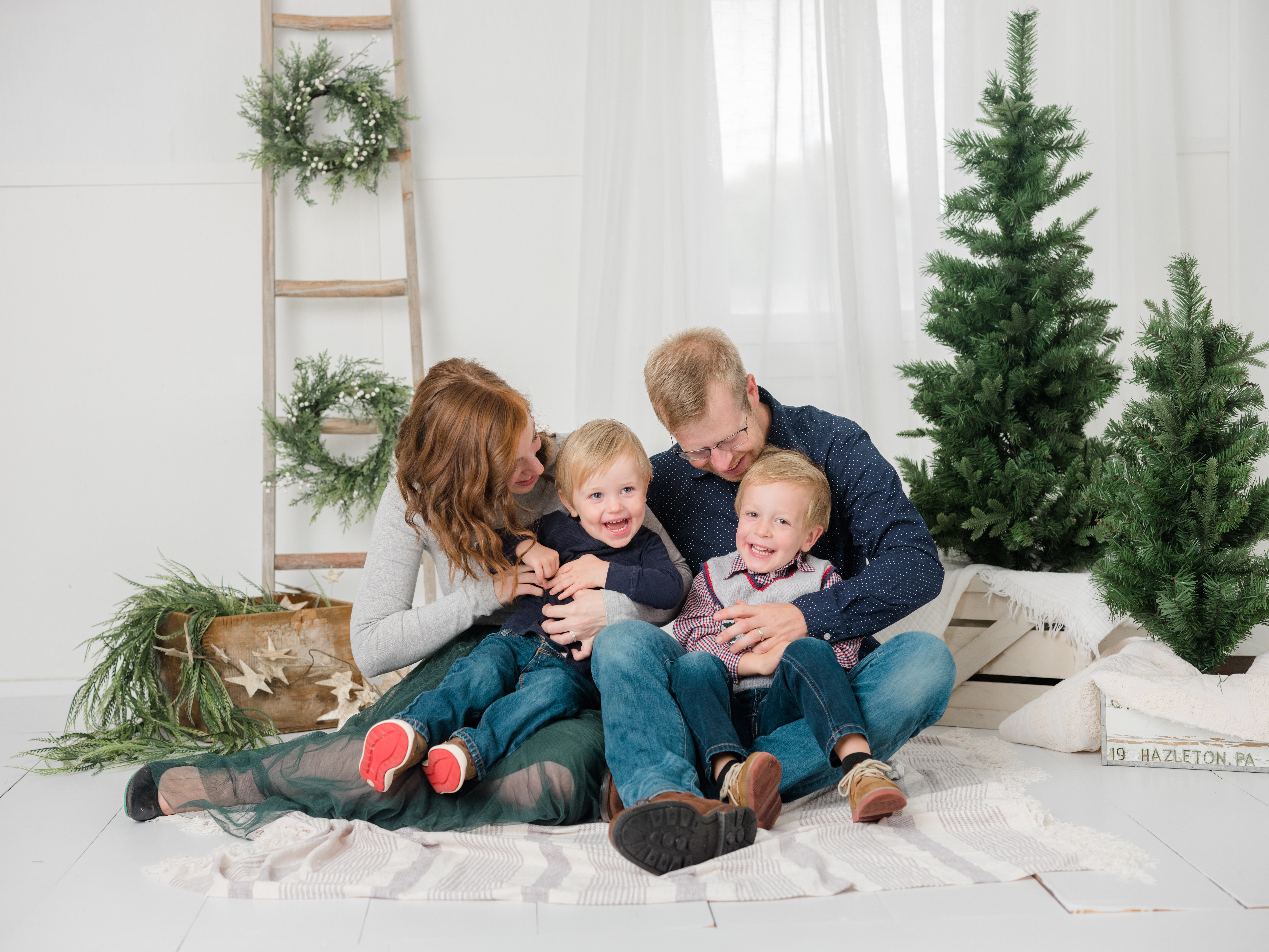 Mom and dad with 2 young boys in picture with christmas trees