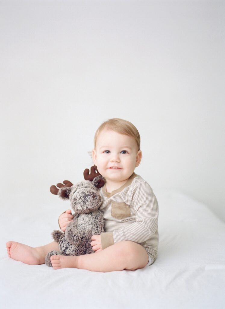 Toddler boy sitting with stuffed moose during milestone mini session in Fisher Illinois
