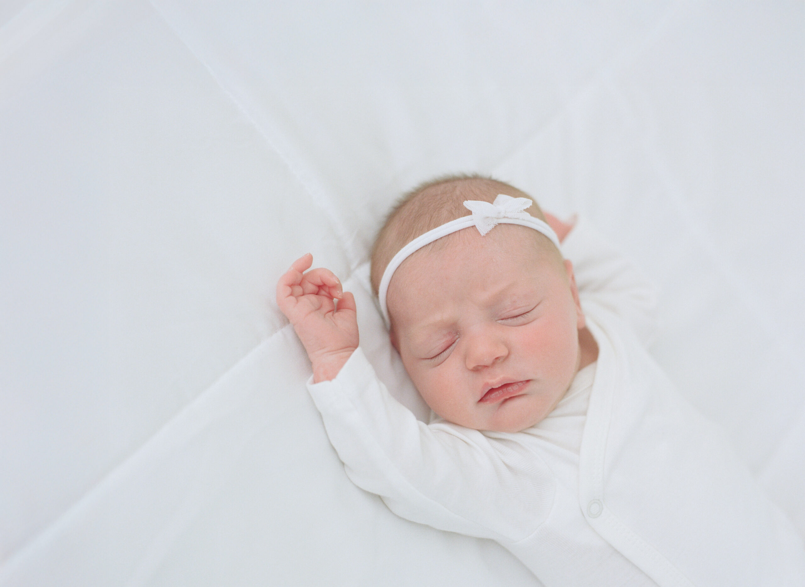 newborn baby in white onesie on white bed in white studio