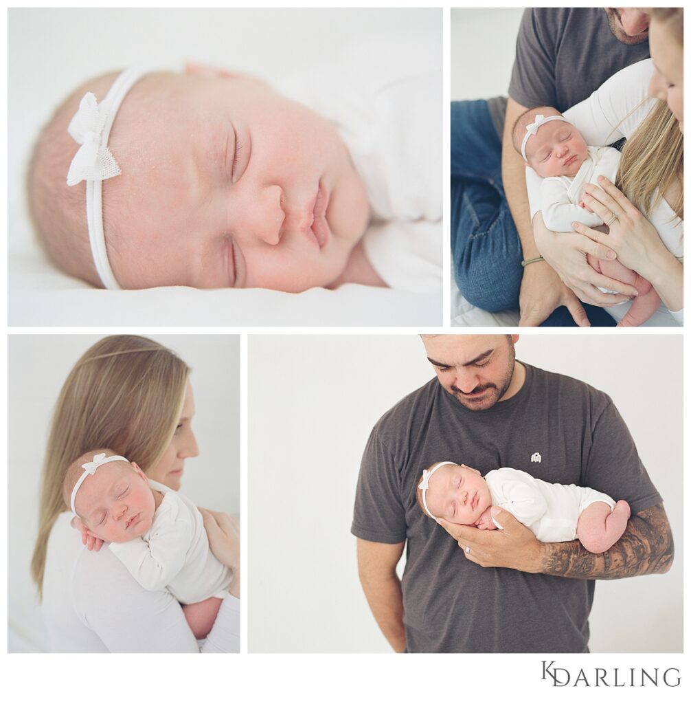 Baby in white onesie on white bed using baby led posing.  Parents holding newborn.  mom holding newborn on shoulder.  Dad holding newborn in arm with a sleeve of tattoos.