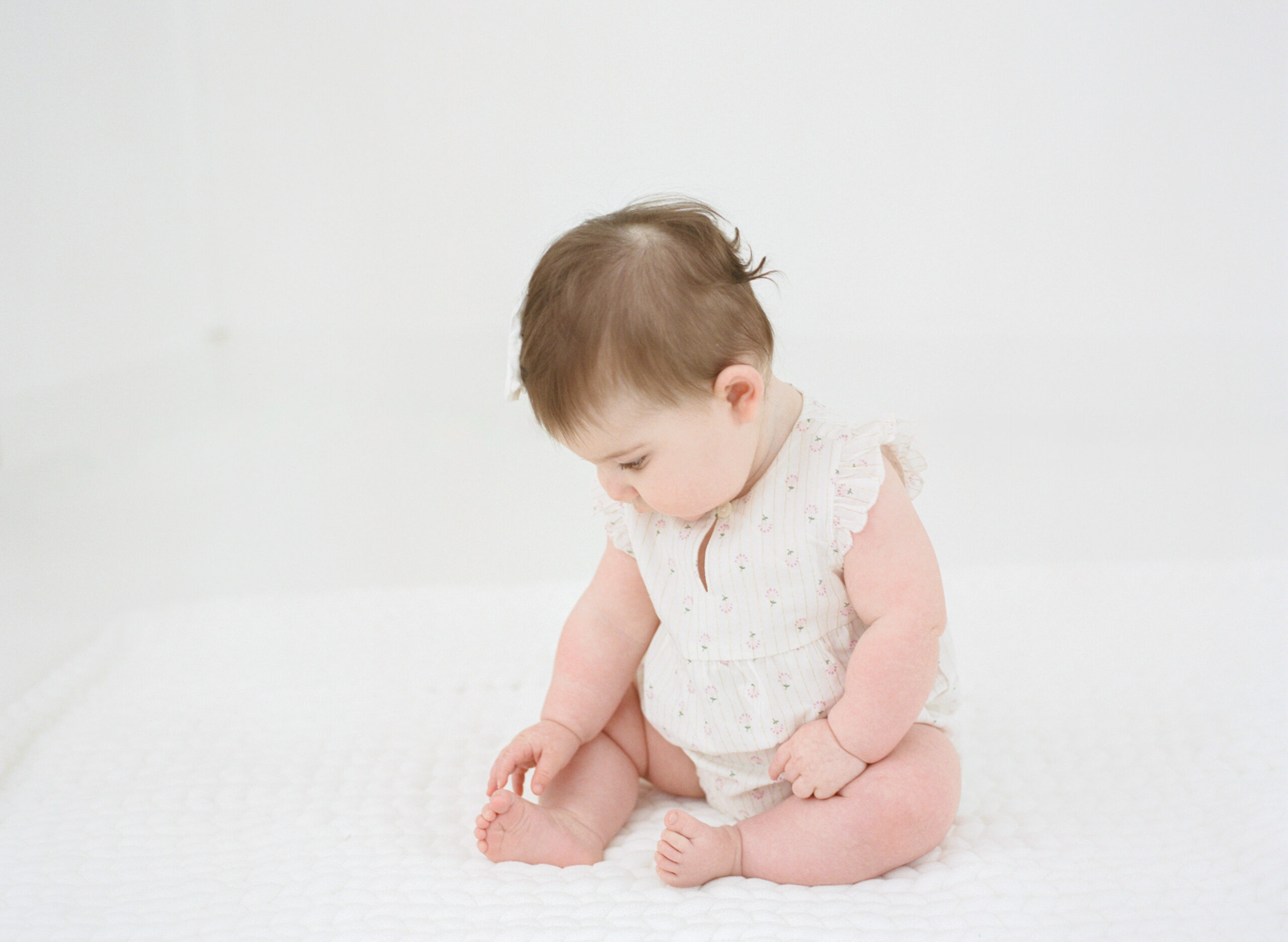 Baby girl sitting on white quilt during milestone photo session in Fisher IL studio